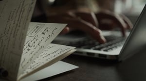 Persona transcribiendo texto de una libreta a una computadora para la realización de contenido | House of Films